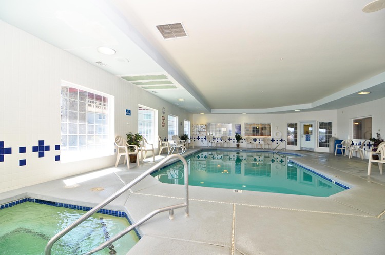 Indoor pool, hot tub, and seating area with white chairs